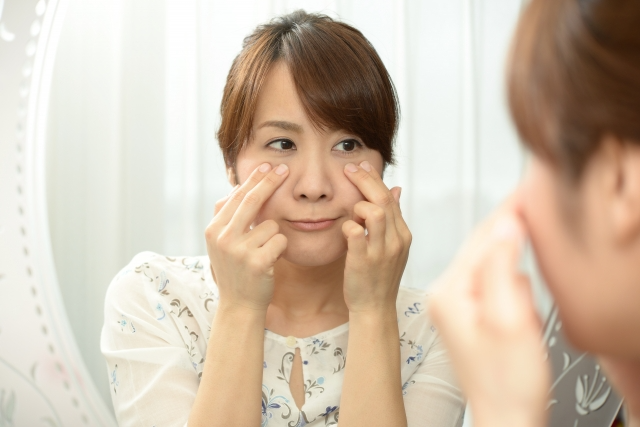 目の下を触り、鏡を見る女性